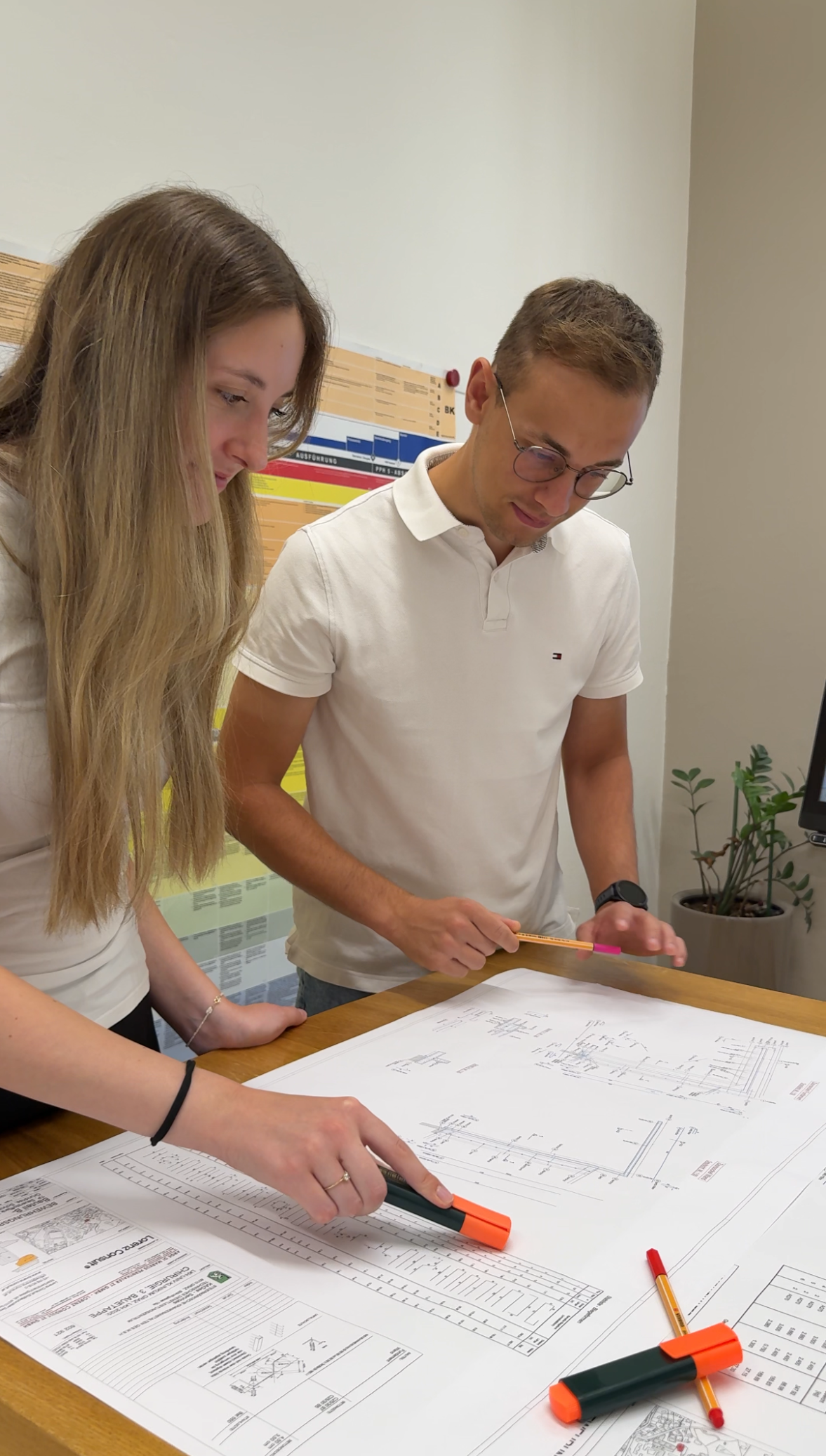 zwei Praktikanten lehnen sich über einen Plan und diskutieren